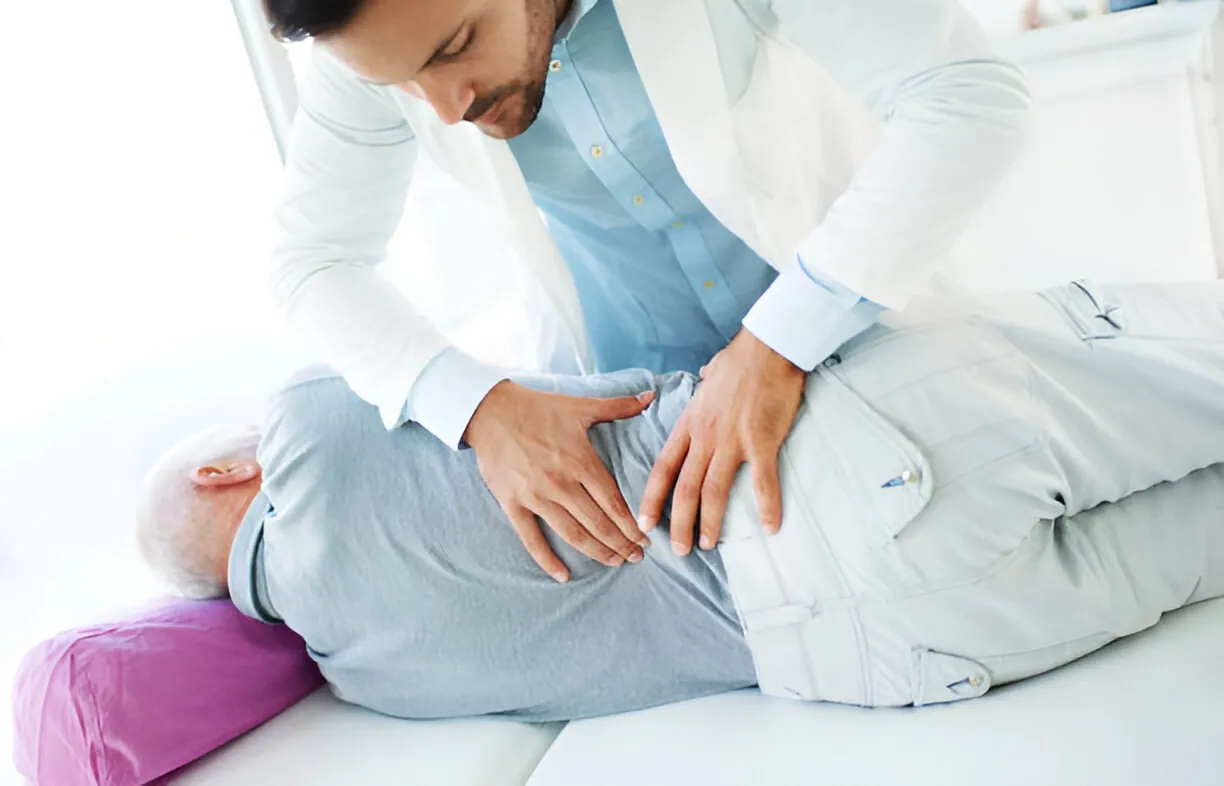 A male doctor or therapist performing a hands-on adjustment or examination of an older male patient's lower back. This image represents effective Pain Management Port St Lucie strategies.
