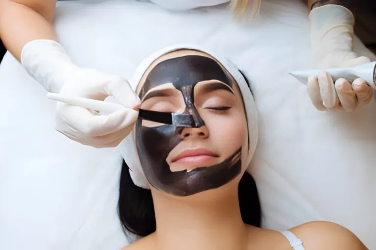 Esthetician applying a deep-cleansing black facial mask to a client as preparation for advanced laser and aesthetics procedures.