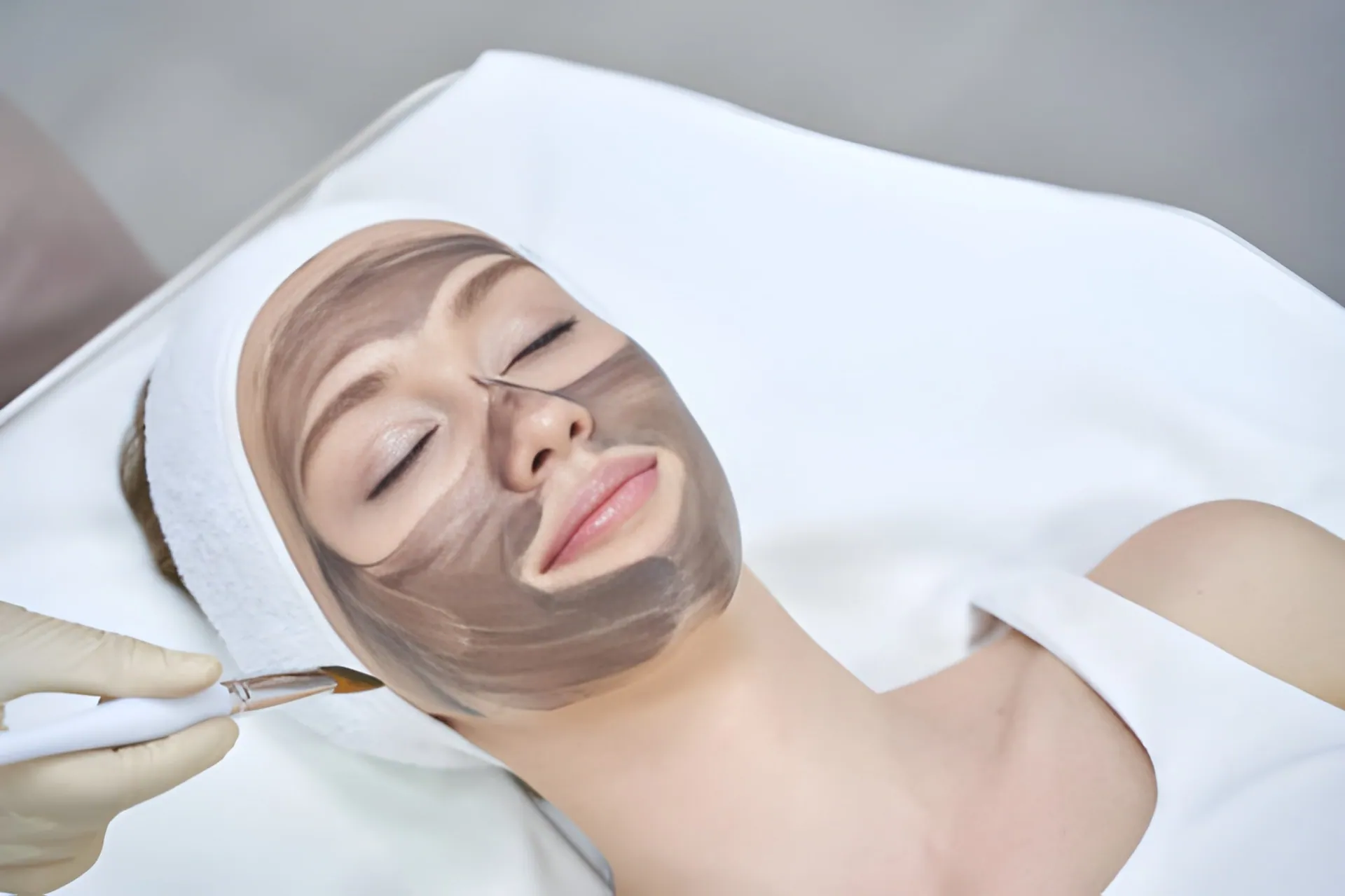 Woman receiving a professional clay facial mask as part of a skincare and laser aesthetics preparation treatment.